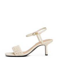Sandale à talons beige avec une bride tissée et une boucle de cheville réglable. Matériau lisse avec un léger éclat et un talon aiguille élancé.