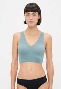 Lysblå sømløs bralette med V-hals og brede stropper; glat tekstur, uden lukninger. Kombineret med sort undertøj.