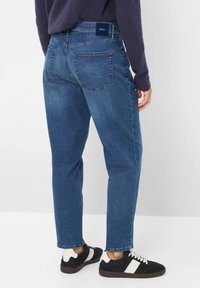 Jeans in denim blu con taglio dritto, dotati di due tasche posteriori e un'etichetta a contrasto in vita, abbinati a sneakers nere e bianche.