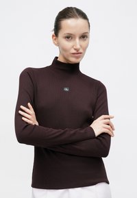 Ciemnobordowa, długorękawowa bluzka z prążkowanej tkaniny i półgolfem. Posiada małą czarną naszywkę z logo na piersi. Prosty, płaski dół.