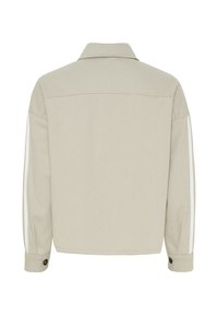 Lys beige houndstooth-jakke med krave, lange ærmer og to hvide striber på ærmerne. Knaplukning ved manchetterne. Glat tekstur.