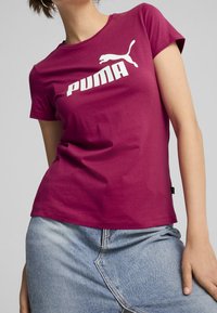 Magenta tričko s krátkým rukávem z bavlny, se silným bílým logem Puma. Mírně obtáhnutý střih s kulatým výstřihem.