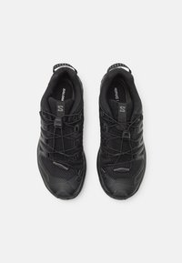 Scarpe sportive nere con parte superiore in rete, sovrastrutture sintetiche testurizzate, lacci elastici e una robusta suola in gomma. Branding discreto sul lato.