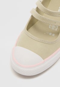 Zapato de lona color beige claro con dos tiras ajustables, punta de goma blanca y detalle de goma rosa en la suela. Suela interior texturizada.