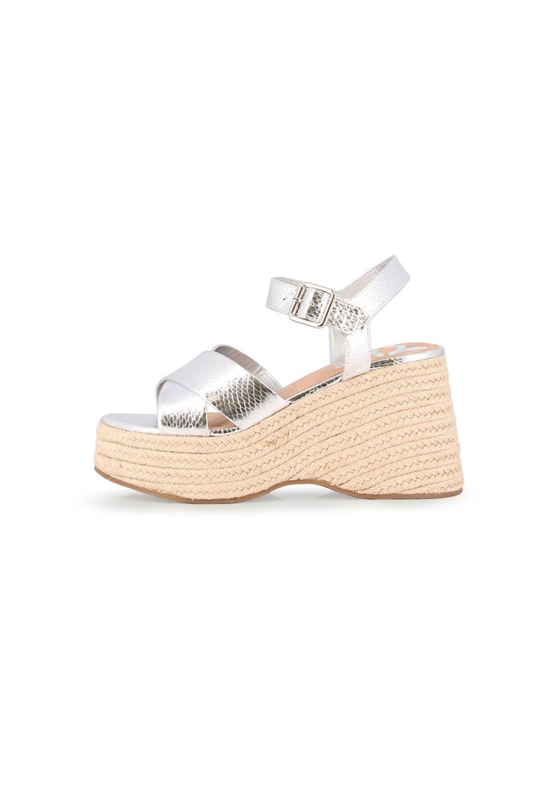 Sandalias de cuña metálicas plateadas con plataforma de yute trenzado. Presenta un diseño de tiras cruzadas y hebilla ajustable en el tobillo.