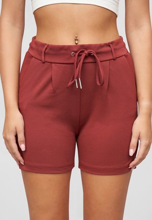 Shorts bordeaux en tissu doux, avec taille à cordon, plis et texture lisse. Longueur jusqu'au milieu de la cuisse. Détails en métal argenté.