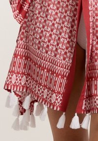 Sarkans kimono ar baltām ģeometriskām apdrukām, ar baltajiem pušķiem apakšmalā. Viegls audums ar atvērtu priekšu un brīvu piegriezumu.