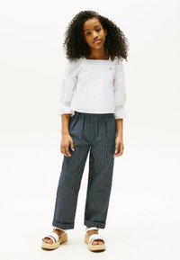 Blusa bianca con texture e maniche a tre quarti abbinata a pantaloni larghi a righe blu navy. Sandali platform bianchi completano l'outfit.
