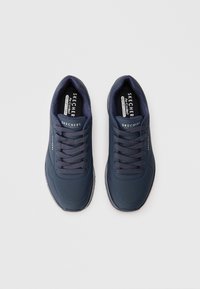 Navy blue Skechers sneakers with a smooth synthetic upper, textured perforations, lace-up design, and cushioned insoles.
