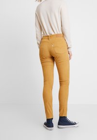  Jeans skinnies de pana amarillos con un diseño de bolsillo trasero, combinados con zapatillas altas marinas. Los detalles adicionales incluyen una etiqueta en la cintura.