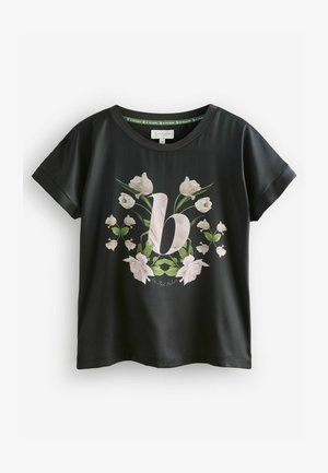 Czarny t-shirt z krótkim rękawem z kwiatowym wzorem, na którym wyraźnie widać różową literę "b" otoczoną białymi kwiatami i zielonymi liśćmi.