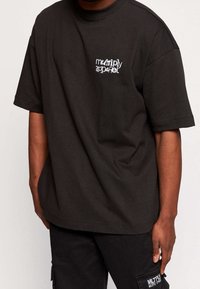 Black cotton t-shirt with short sleeves, loose fit, and a white graphic logo reading "multiply apparel" on the left chest.