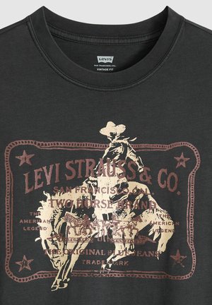 Black cotton t-shirt featuring a vintage-style graphic in bronze, depicting a cowboy on a horse with detailed text and borders.