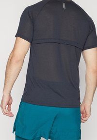 Krátký rukáv sportovního trička v tmavě šedé barvě s texturovaným vzorem. Obsahuje vodorovný šev na zádech a slim fit pro pohodlný pohyb.