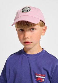Rosa Baseballkappe mit einem runden schwarzen Emblem, getragen mit einem lila Rundhals-T-Shirt, das ein kleines rotes Logo auf der Brust aufweist.