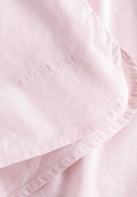 Lichtroze katoenstof met een gladde textuur, voorzien van een geborduurd "STUDIO FEDER" logo. Randen zijn netjes gestikt.