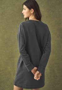 Robe-sweatshirt surdimensionnée gris charbon fabriquée en tissu doux. Présente une coupe décontractée, des manches longues et des poignets côtelés. Design minimaliste.