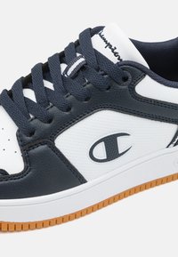 Baskets de sport en cuir marine et blanc avec des accents texturés, bout rond, semelle en caoutchouc et lacets noirs. Présente un logo sur le côté et la languette.