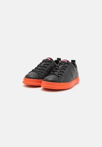 Baskets en cuir noir avec une semelle en caoutchouc orange, présentant un bout rond, des perforations et un laçage plat. Logo rouge sur la languette.