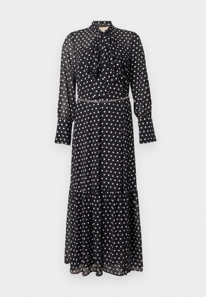 Zwarte midi-jurk met lange mouwen en witte polka dots, hoge hals met strik, manchetten aan de mouwen en een dun zilveren kettingriem.