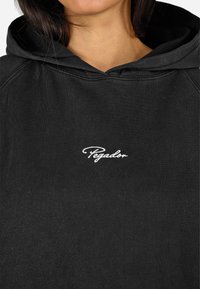 Čierna mikina s kapucňou vyrobená z texturovanej bavlny, so výrazným bielym výšivkovým logom "Pegador" na prednej strane. Klasický dizajn s kapucňou na šnúrku.