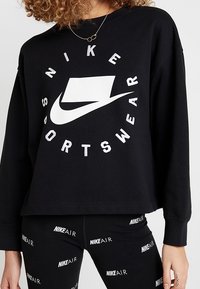 Black sweatshirt with white "NIKE" and "SPORTSWEAR" text graphic, crew neckline, and long sleeves, paired with black leggings featuring "NIKE AIR" print.