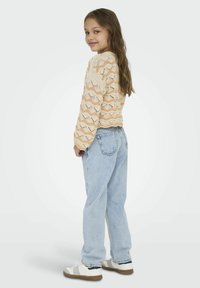 Crème en perzik gebreide trui met zigzagpatroon, full-length lichtblauwe denim jeans en witte sneakers met donkere accenten.