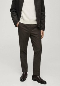 Braun melierte Wolle-Hosen mit schlankem Schnitt und feiner Textur. Kombiniert mit einem cremigen Pullover und dunkelbraunen Ankle Boots.