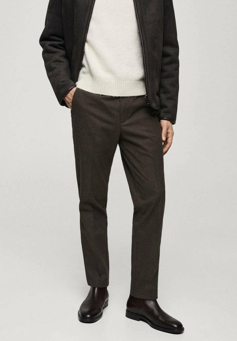 Braun melierte Wolle-Hosen mit schlankem Schnitt und feiner Textur. Kombiniert mit einem cremigen Pullover und dunkelbraunen Ankle Boots.