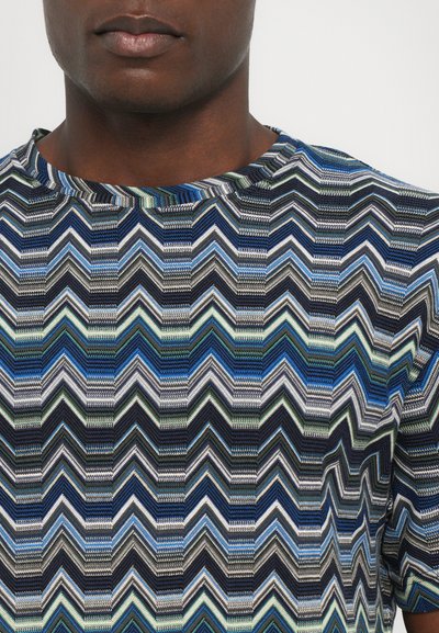 Chemise à manches courtes avec un motif en chevron dans des nuances de bleu, vert et gris, fabriquée dans un tissu texturé avec une coupe décontractée.