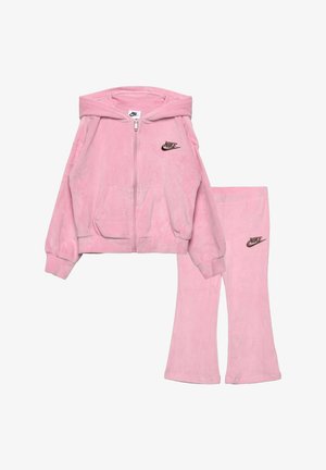 Ensemble en velours rose de Nike comprenant un sweat à capuche et un pantalon assorti, avec poches avant et logos Nike noirs sur la poitrine et la cuisse.