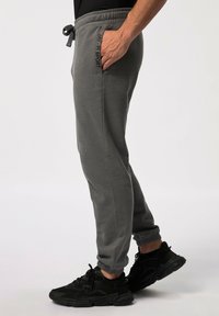 Grijze joggingsbroek met een elastische tailleband, zijzak en omgeslagen pijpen, gecombineerd met zwarte sportschoenen met gaasaccenten.