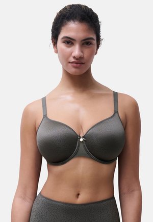 Donna con capelli scuri e ricci che indossa un reggiseno grigio con motivo coordinato e biancheria intima a vita alta su uno sfondo bianco neutro.