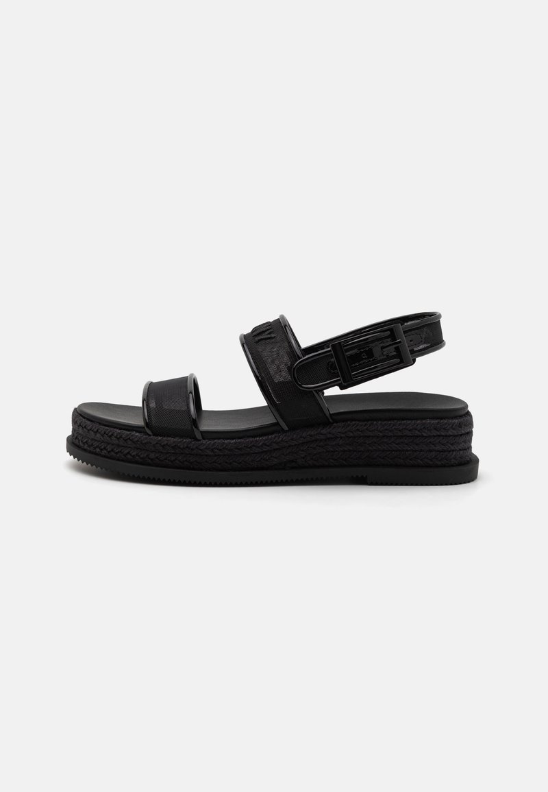 Black sandals with a textured upper, featuring two wide straps and an adjustable ankle strap, set on a braided platform sole.