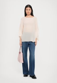Ljusrosa genomskinlig topp med vida ärmar, parat med mörkblå utsvängda jeans och en ljusrosa handväska. Slät textur, avslappnad passform.