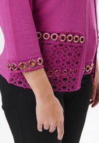 Fuchsia Cardigan mit einem strukturierten Spitzenrand und runden goldenen Ösen. Lange Ärmel mit Spitzenakzenten an den Bündchen.