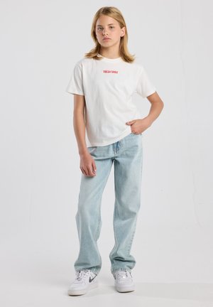 Weißes Baumwoll-T-Shirt mit rotem "FRESH DAILY"-Aufdruck, kombiniert mit hellen Jeans im geraden Schnitt und weißen Sneakern mit schwarzen Akzenten.