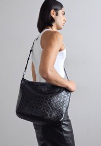 Borsa a tracolla nera in pelle con un motivo geometrico testurizzato, dotata di una sola tracolla e di un ampio interno liscio.