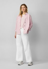 Jasnoróżowa, oversize'owa kurtka dżinsowa, biała koszulka z grafiką w paski, białe spodnie o szerokich nogawkach i szare sneakersy z akcentami.