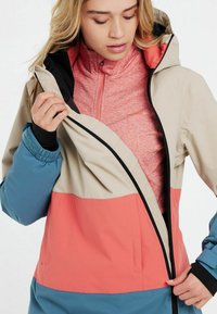 Bunte Jacke mit einem beigen oberen Teil, einem pinken mittleren Teil und einem blauen unteren Teil; verfügt über einen Reißverschluss vorne, eine Kapuze und ein inneres Fleecefutter.