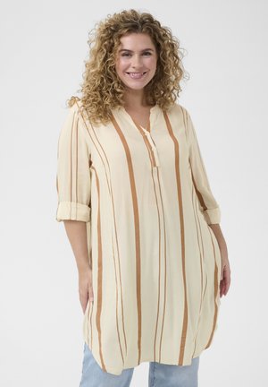 Lichtbeige tuniek met verticale bruine strepen, knoopsluiting in v-hals en opgerolde mouwen. Gemaakt van een zachte, lichte stof.