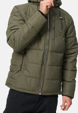 Personne portant une veste matelassée vert olive avec fermeture éclair frontale et poche poitrine, réglant le col de la veste d'une main.