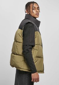 Puffervest med en sort overdel og olivengrøn underside, med høj krave og quiltet mønster, lavet af skinnende nylonmateriale.