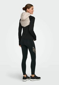 Črna športna majica z dolgimi rokavi in bež prešito kapuco, kombinirana s črnimi pajkicami z leopardjim vzorcem na strani.