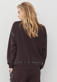 Tumepruun särk, millel on mugav lõike, tekstuuriga mustad aksendid õlgadel ja serval ning soonikuga ümbrised sujuva viimistlusega.