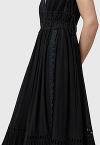 Abito nero con un design fluido, caratterizzato da tessuto testurizzato, pizzo decorativo, vita arricciata e morbide pieghe, che ne esaltano l'eleganza.