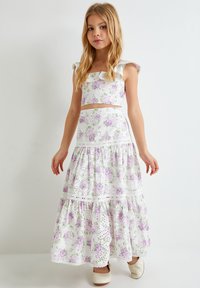 Top court floral blanc et jupe maxi à volants avec des roses violettes et des feuilles vertes. Présente des détails en œillets et des manches à volants.