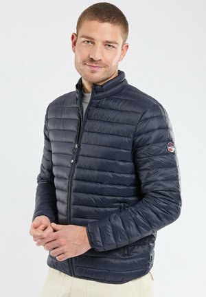 Veste matelassée bleu marine avec design quilté horizontal, col haut, poches latérales et logo sur la manche gauche. Tissu lisse et léger.