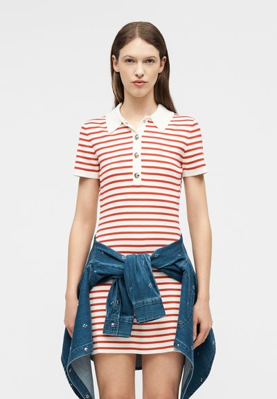 Γυναίκα που φοράει κοντομάνικο φόρεμα με κόκκινες και λευκές ρίγες, με λευκό γιακά και τζιν μπουφάν δεμένο γύρω από τη μέση της.