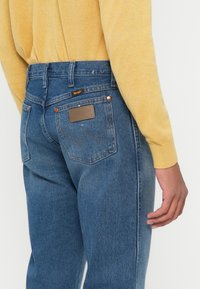 Blå denim jeans med rett snitt, med et lærpatch på baksiden, kontrasterende sømmer og koperfinnede detaljer.